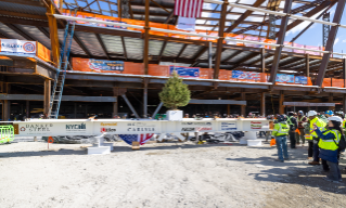 Construction workers gather at a construction site for the new Terminal One, with a banner displaying company logos and an American flag overhead.