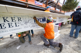 Construction workers signing a steel beam at a building site, showcasing various signatures and markings.