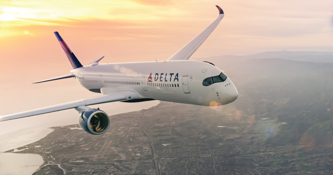 A Delta Airlines airplane flying above a landscape during sunset.