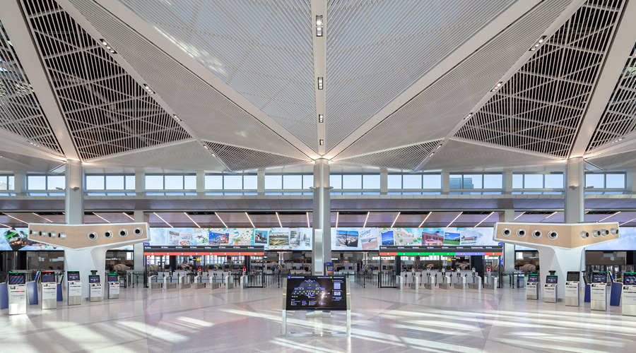 A spacious airport terminal interior featuring modern design elements, check-in counters, and large digital displays.