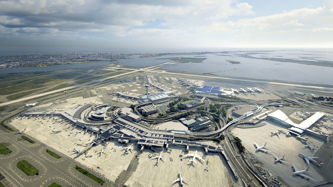 Aerial view of a large airport with multiple runways and parked aircraft, surrounded by water and cityscape in the background.