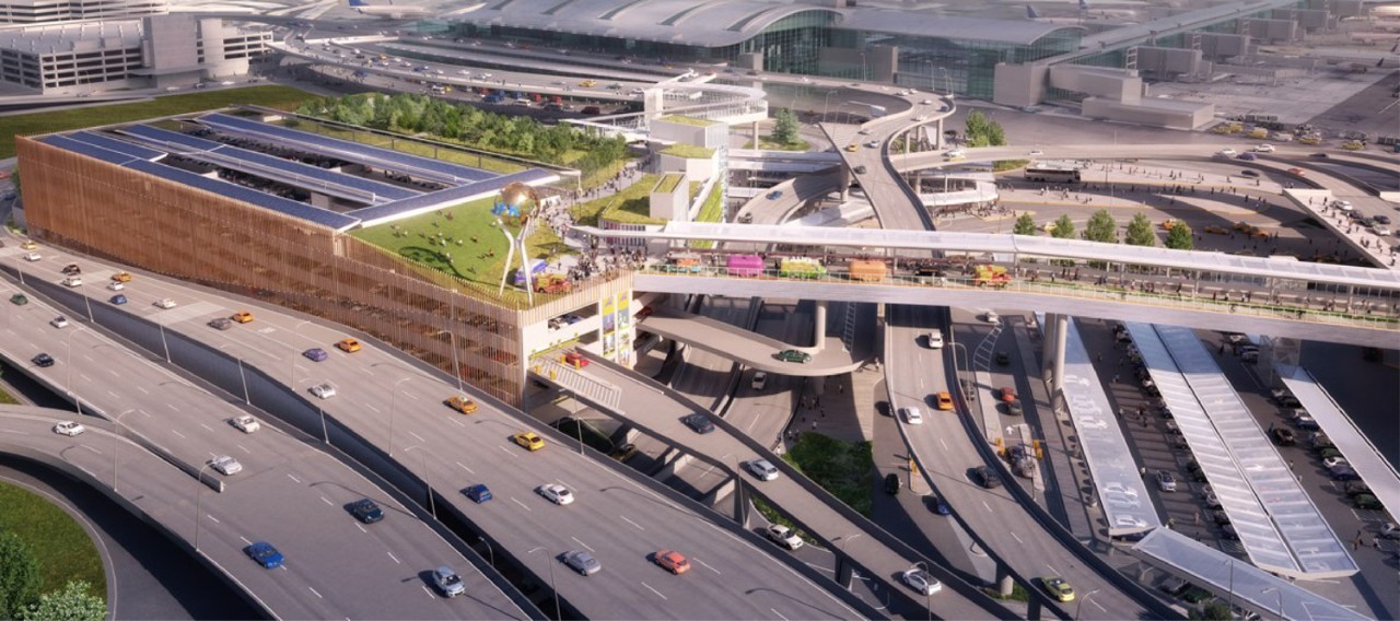 Aerial view of a modern transportation hub featuring a green rooftop, solar panels, and multiple roadways with vehicles.