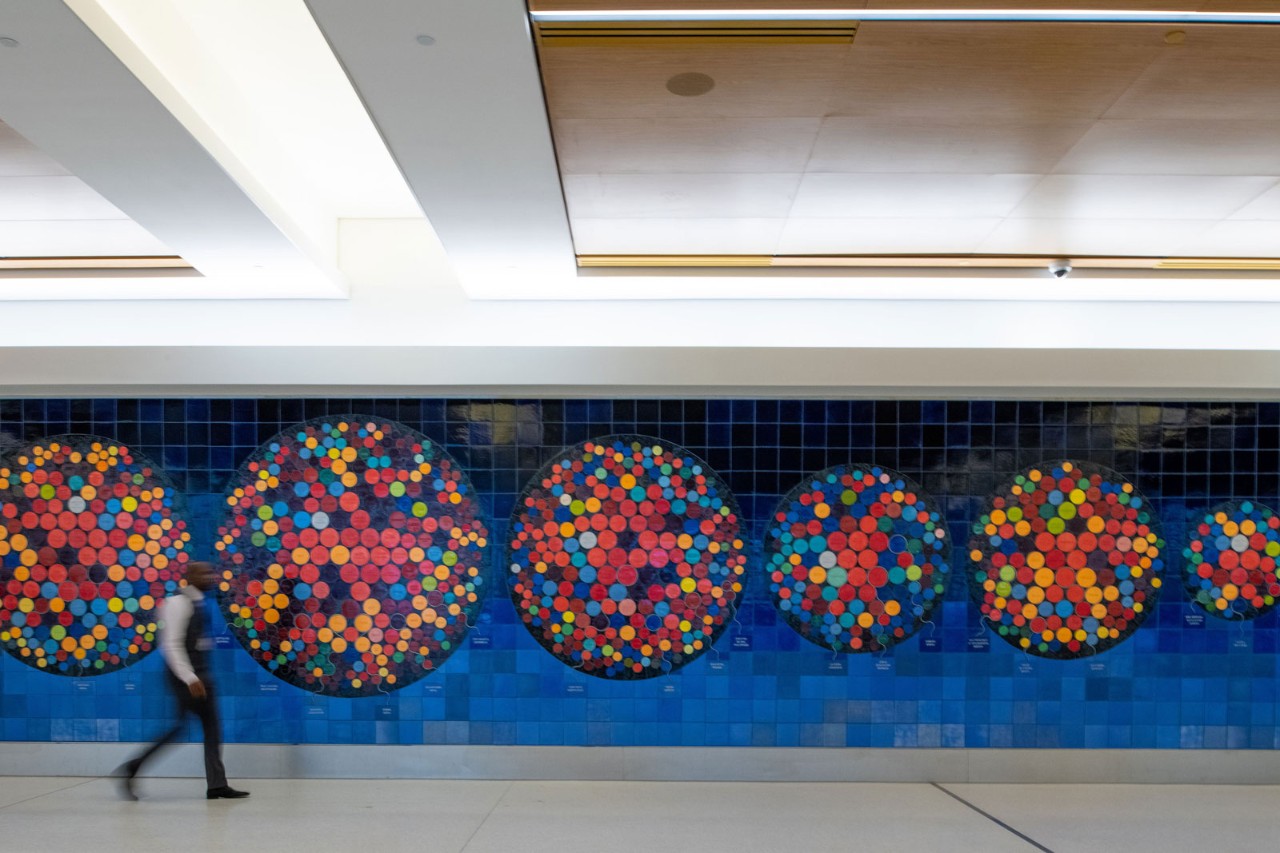 A colorful wall installation featuring multiple circular patterns composed of various colored dots against a blue background.