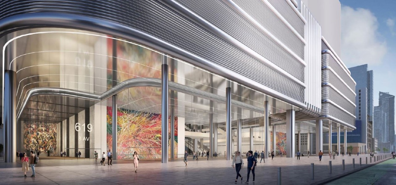 A modern urban building featuring large glass facades and colorful artwork displayed at the entrance. People are walking around the area.